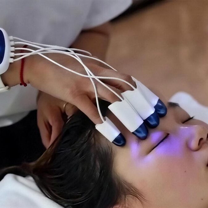 A Pamperloft therapist works violet-blue light fingertip caps across a relaxed guest's forehead during the Deep Sleep Head Therapy, a head massage-inspired brain anti-aging treatment